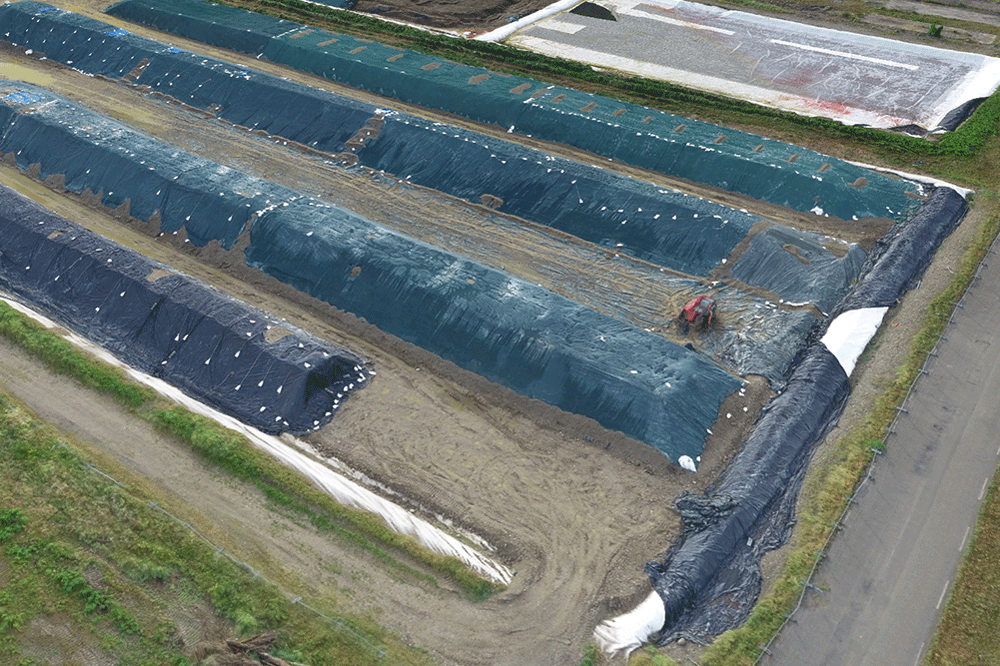 Vue oblique modélisée via un drone d’un chantier de terrassement avec des zones recouvertes de bâches blanches, du matériel de construction et des engins de chantier, pour analyser des volumes de terre.